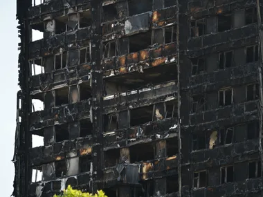 Charred remains of Grenfell Tower after the tragic fire, showing multiple burnt-out floors and windows, against a clear sky.
