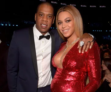 A couple embracing at a formal event, with one wearing a red sequined dress and the other in a tuxedo.