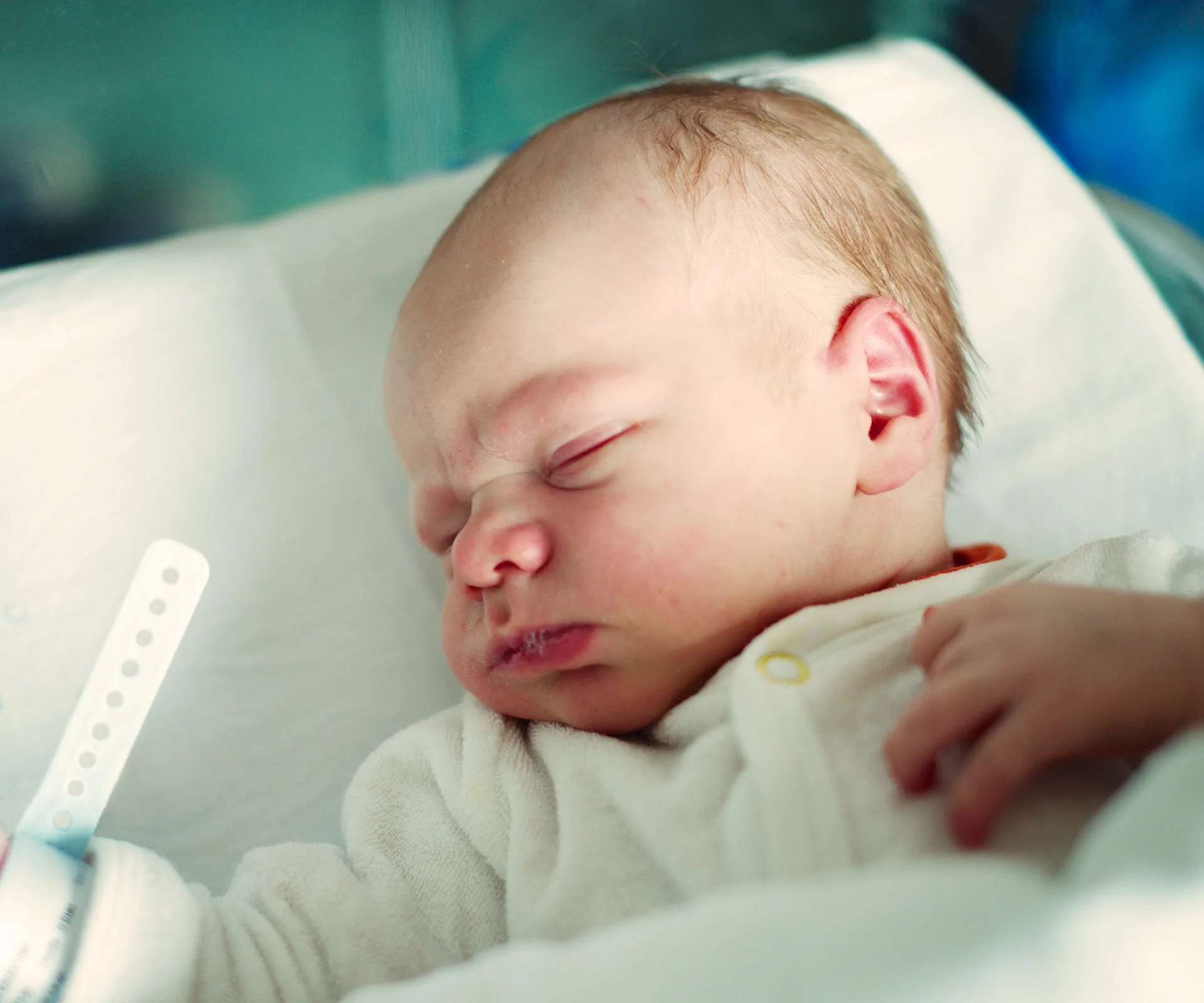A newborn baby sleeping in a crib, wearing a white onesie and hospital wristband, peaceful and serene.