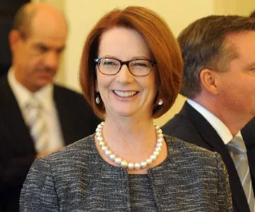 Smiling woman with glasses and pearl necklace at a formal event.