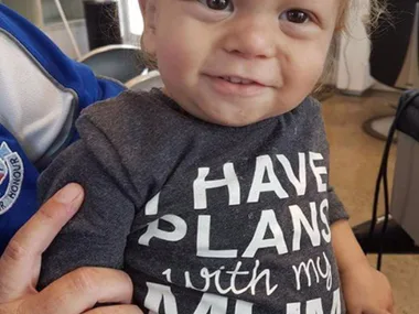 A smiling toddler wearing a shirt that reads "I have plans with my mum."