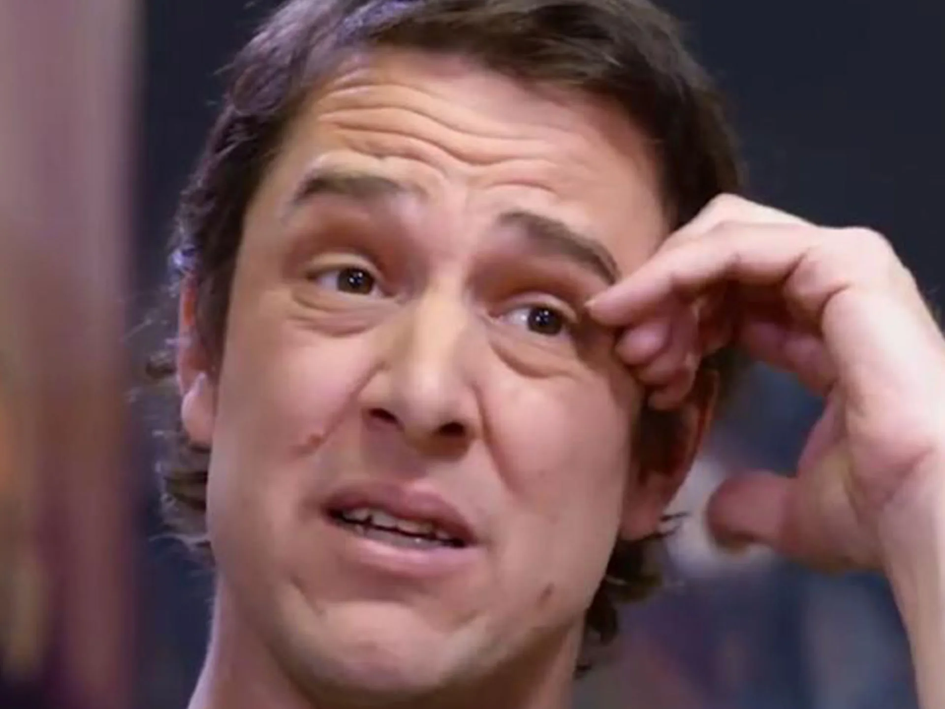 A person appears emotional, looking upwards with one hand on their forehead, possibly during a conversation or interview.