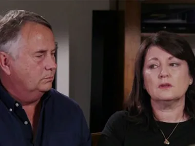 Two people sitting together, looking serious and engaged in a conversation indoors.