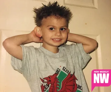 Young child with spiky hair and a gray T-shirt, smiling with hands behind head; NW logo in corner.