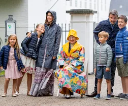 Danish royal family smiling in rain with colorful raincoats، posing at an outdoor event.