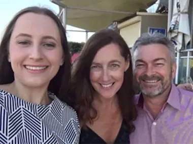 A smiling group of three people taking a selfie outdoors on a sunny day.