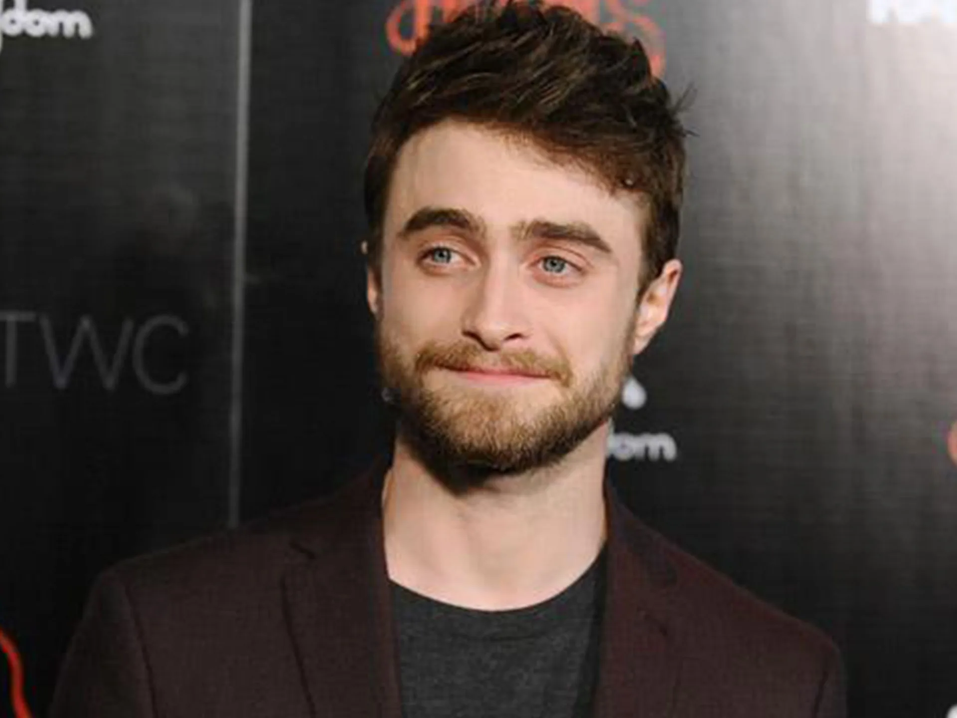 A person with a beard and short brown hair smiles slightly at an event, against a dark background with red text.