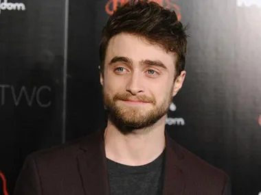 A person with a beard and short brown hair smiles slightly at an event, against a dark background with red text.