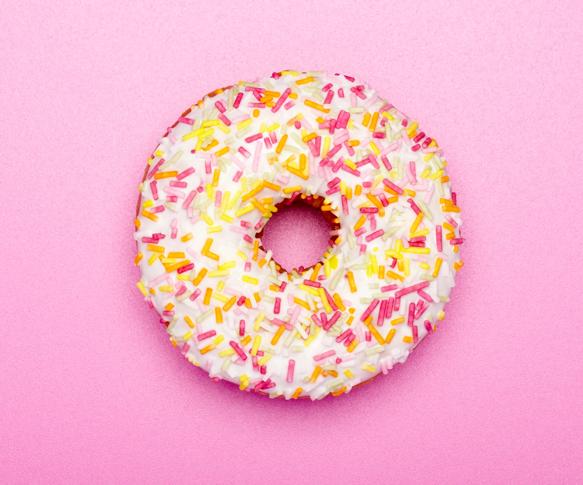 Colorful sprinkled donut on pink background.