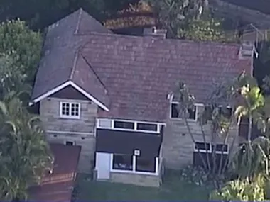 Aerial view of a stone house with a brown tile roof surrounded by trees and greenery.