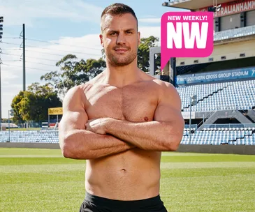 A shirtless athlete stands confidently with crossed arms in a stadium, promoting a "New Weekly" magazine feature.