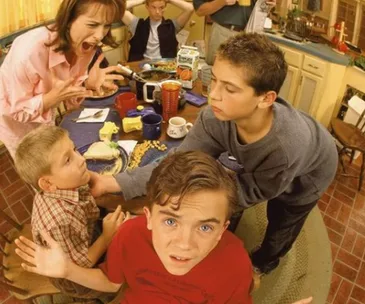 Family chaos at breakfast table; one boy looks confused, mom is yelling, another boy is eating, others look anxious.