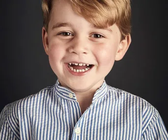 A young child with a bright smile, wearing a blue and white striped shirt, against a dark background.