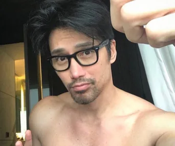 Man with glasses and facial hair taking a shirtless selfie in front of a mirror.
