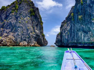 Boat approaching stunning limestone cliffs and turquoise waters in Palawan, Philippines under a bright blue sky.