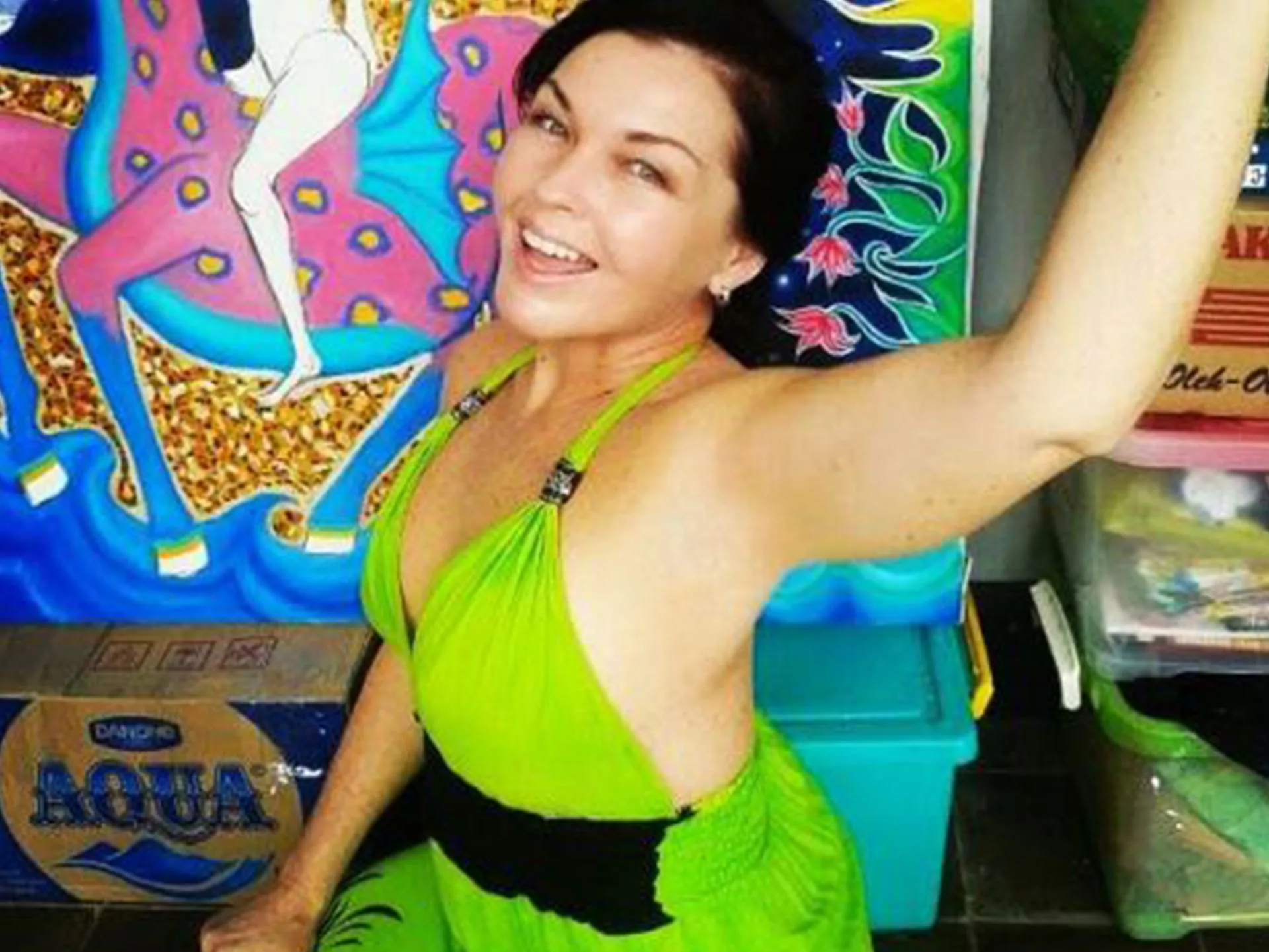 A woman in a green dress poses joyfully in front of a colorful mural, with boxes labeled "AQUA" nearby.
