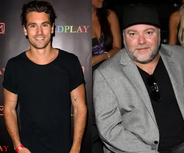 "Two men standing side by side at an event; one in a black t-shirt, the other in a gray jacket and black cap."
