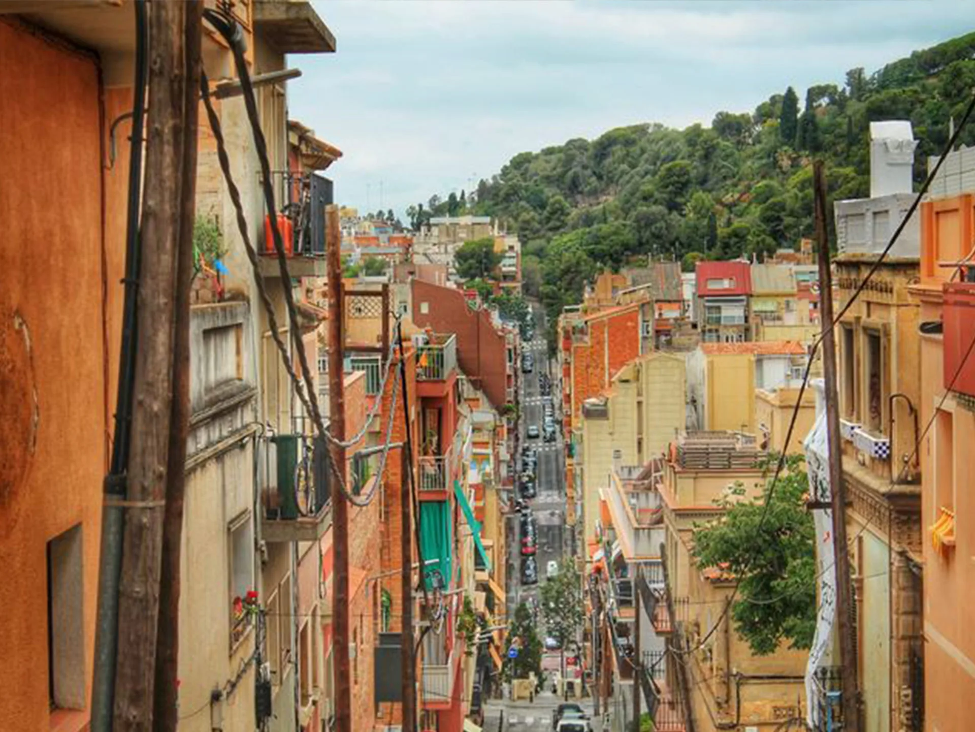 A view of a narrow street lined with colorful buildings, leading towards lush greenery in a cityscape.