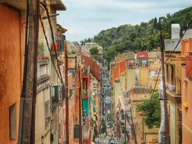 A view of a narrow street lined with colorful buildings, leading towards lush greenery in a cityscape.