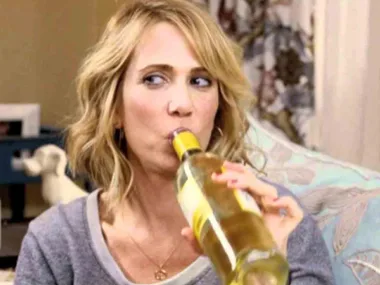 A person sipping wine directly from a bottle with a thoughtful expression on their face.