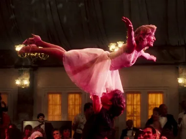 A scene from "Dirty Dancing" showing a woman lifted in a dance pose by a man in a crowded ballroom.
