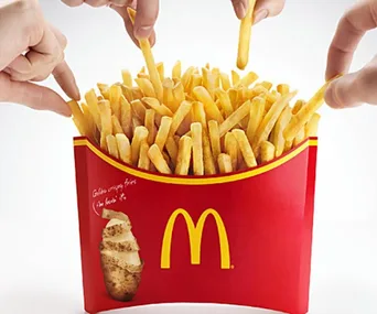 Hands grabbing fries from a large McDonald's fries carton.