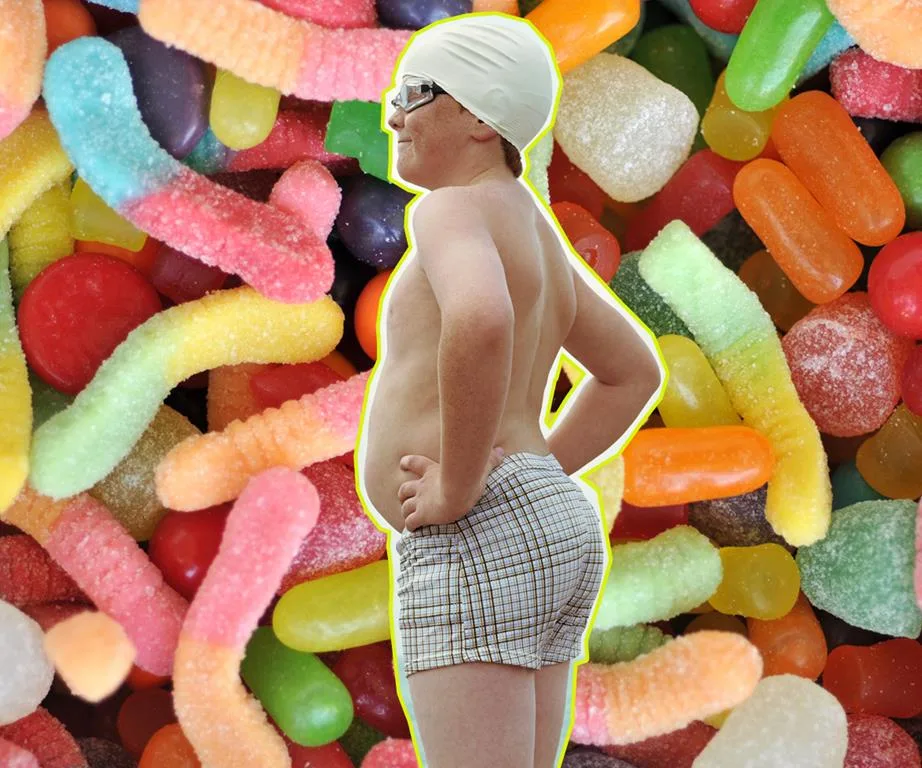 Overweight child in swim cap and goggles stands against colorful candy background.