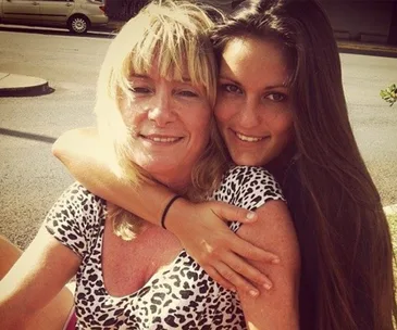 Woman with long hair hugging another woman with short blonde hair and leopard print top, smiling outdoors.