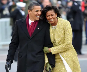 Two people in formal attire, walking together and smiling warmly at an event.