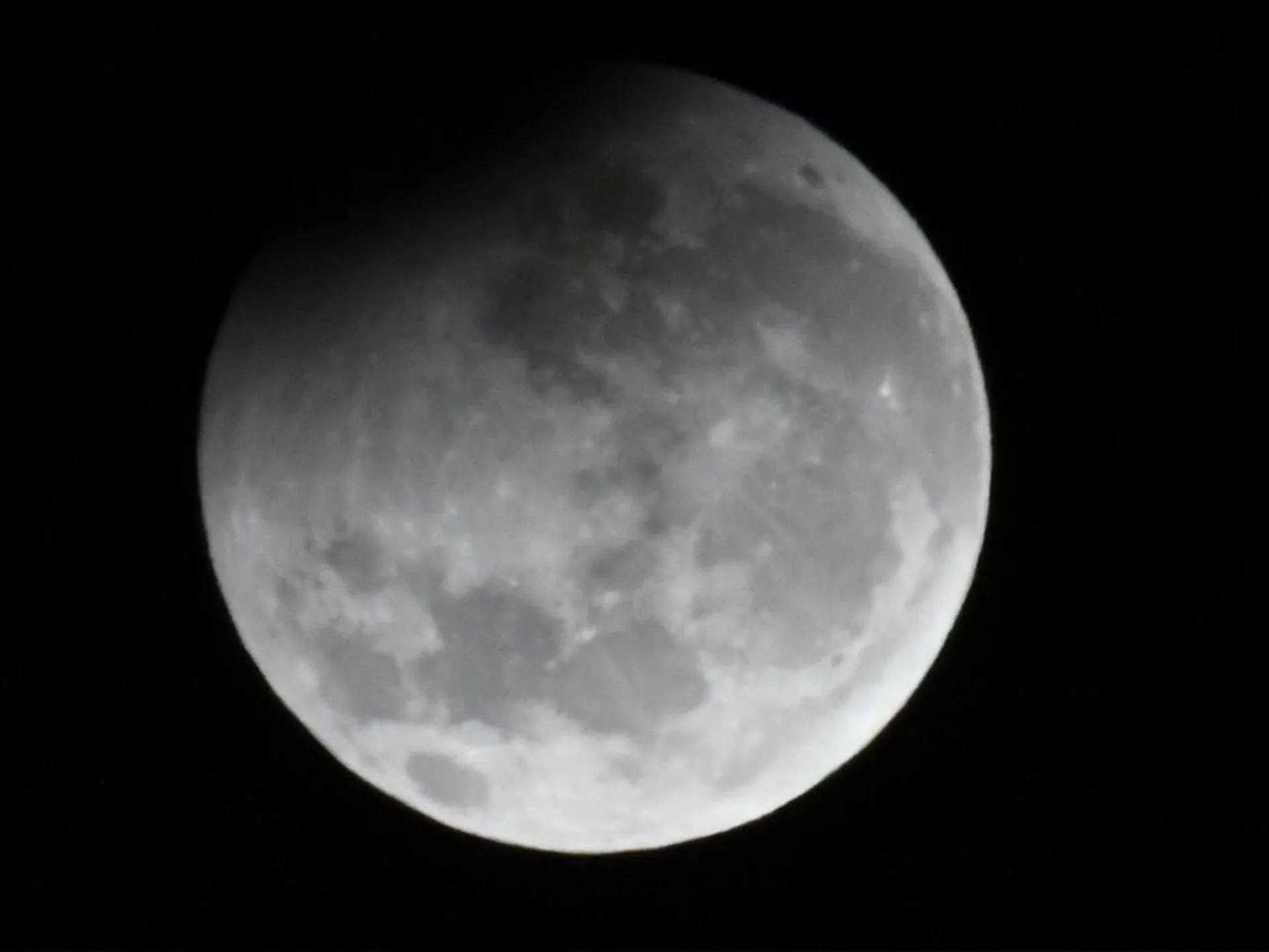 Partial lunar eclipse with shadow on the top-left of the moon against a dark sky.