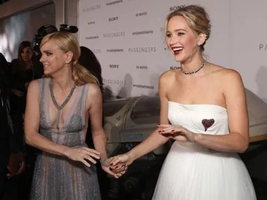 Two actresses smiling and holding hands on the red carpet at the "Passengers" movie premiere.