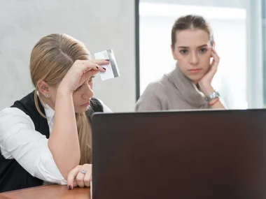 Two concerned women looking at a laptop screen, one holding a credit card.