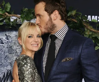 Man kissing woman on forehead at event, both smiling in front of greenery backdrop.