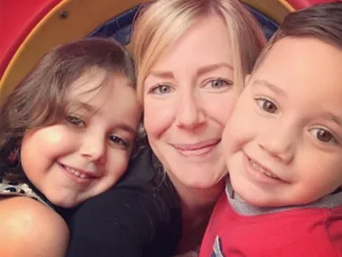 A woman smiling with two children on her sides, all looking at the camera closely.