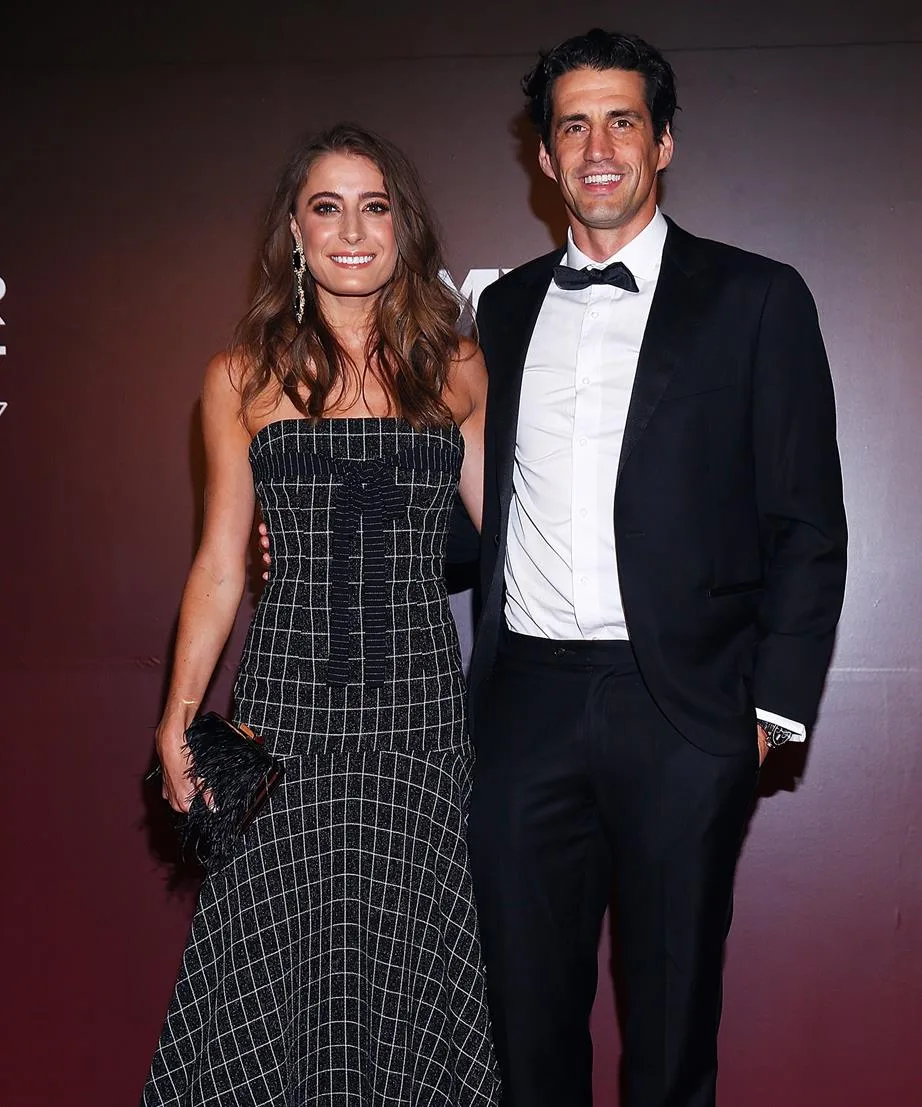 A couple poses elegantly in formal attire, with the man in a tuxedo and the woman in a patterned evening gown.