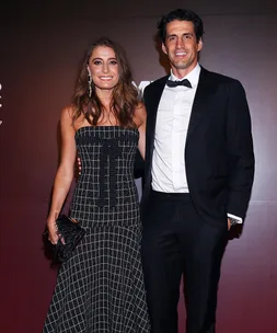 A couple poses elegantly in formal attire, with the man in a tuxedo and the woman in a patterned evening gown.