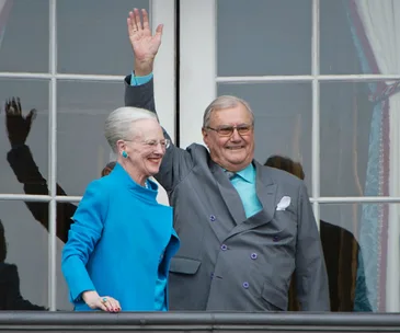 A couple standing on a balcony, smiling and waving at an event.