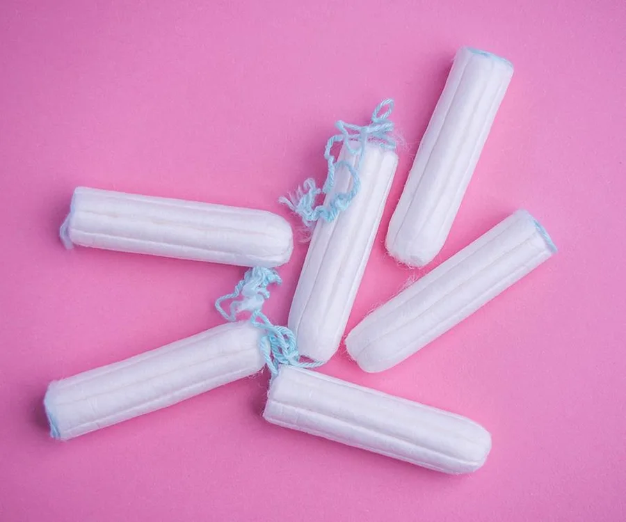 White tampons with blue strings scattered on a pink background.