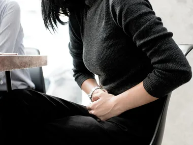 A person in a black sweater sitting, holding their stomach, possibly indicating discomfort or bloating.