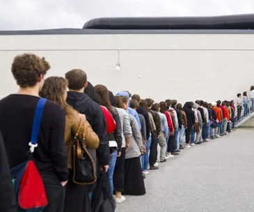 A long line of people waiting outside against a plain wall, showing diverse attire and styles.