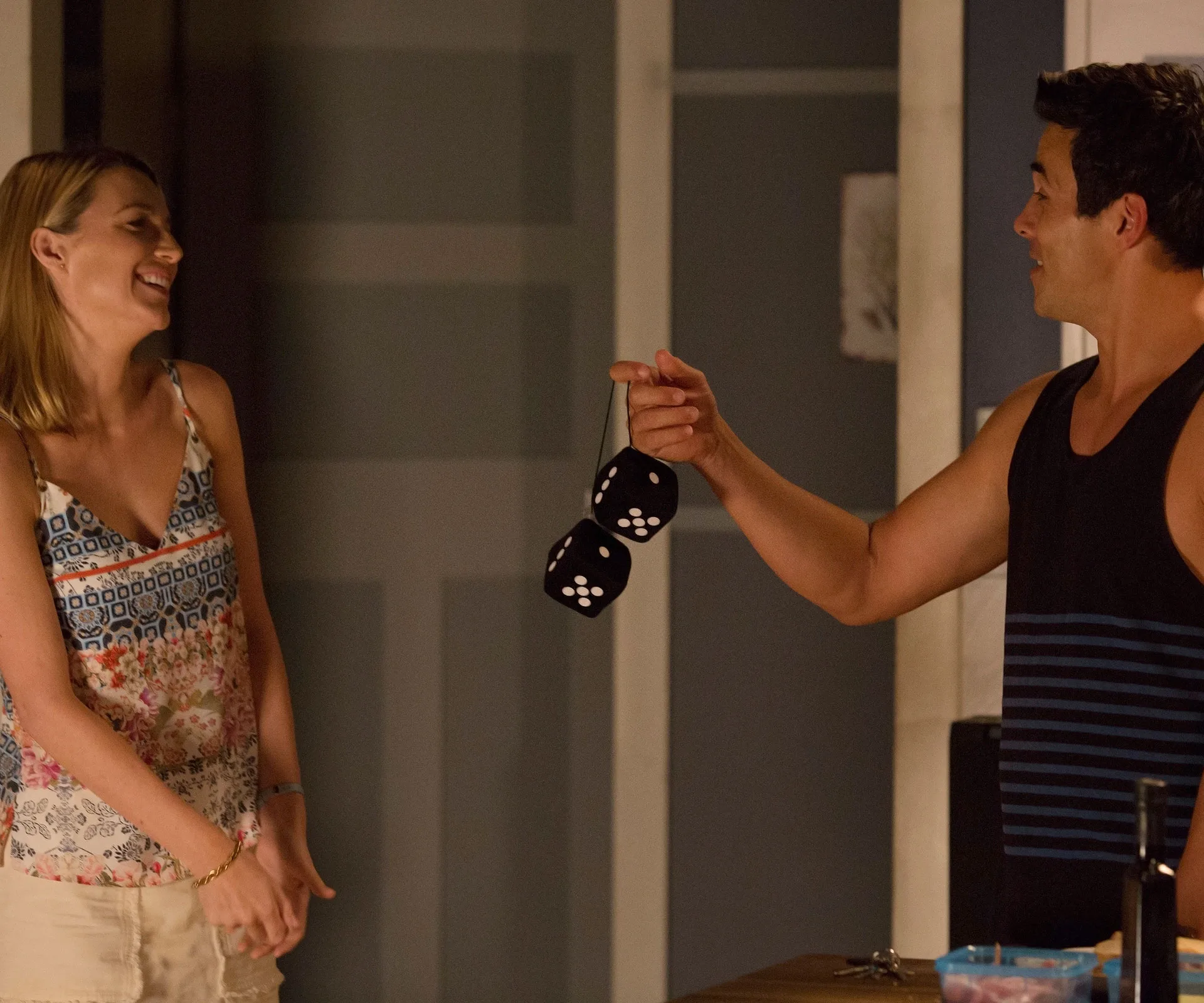 Man holding fuzzy dice while smiling woman watches in a casual setting.
