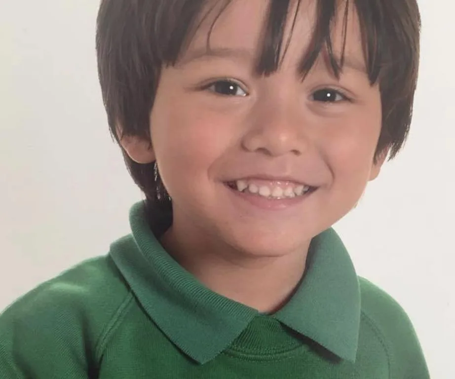 Smiling young boy with dark hair wearing a green shirt.