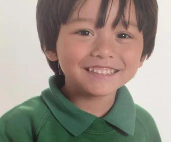 Smiling young boy with dark hair wearing a green shirt.