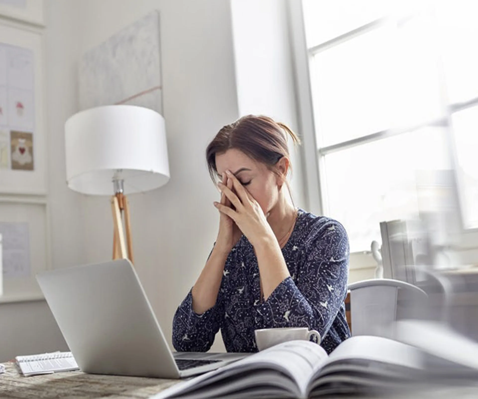 A frustrated woman sitting at a desk with a laptop, holding her head in her hands.