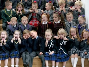 A group of young twins in school uniforms making funny faces on their first day of school.