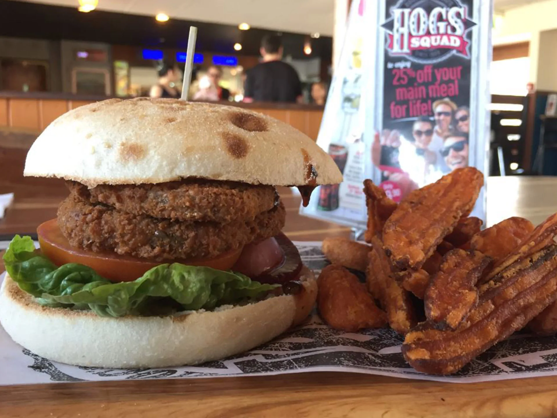 Vegan burger with lettuce and tomato on a rustic bun, served with sweet potato fries at Hog's Breath Cafe.