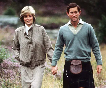 A couple smiling and holding hands while walking outdoors, with greenery in the background.