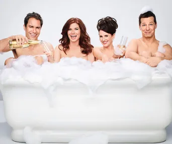 Four people in a bubble bath, two holding champagne glasses, one pouring champagne, all smiling and playful.