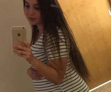A woman with long hair taking a mirror selfie while holding her pregnant belly, wearing a striped shirt.