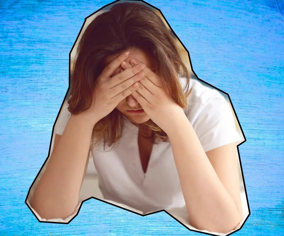 A woman with her head in hands against a blue background, conveying distress or sadness.
